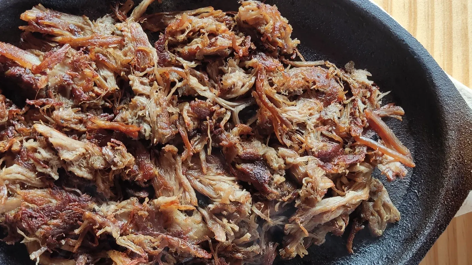 Orden de carne de borrego dorada, deshebrada y crujiente, en cazuela de hierro