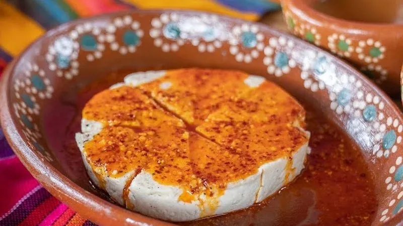 Queso fresco a la plancha bañado en salsa macha, en plato de barro junto a cazuelitas de salsa