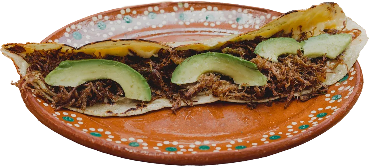 Machete de carne dorada: quesadilla grande de maíz rellena de borrego con láminas de aguacate, en plato de barro