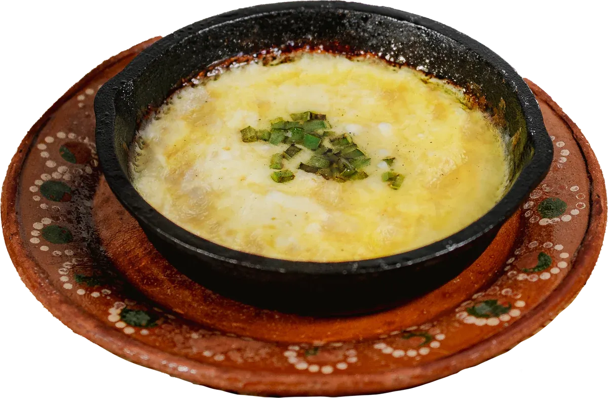 Queso fundido gratinado con cebollín en cazuela de hierro sobre plato de barro