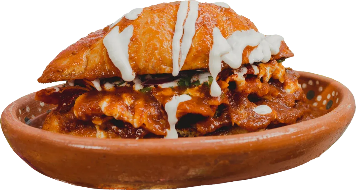 Torta ahogada de borrego en pan birote bañada en consomé picante y crema, en plato de barro
